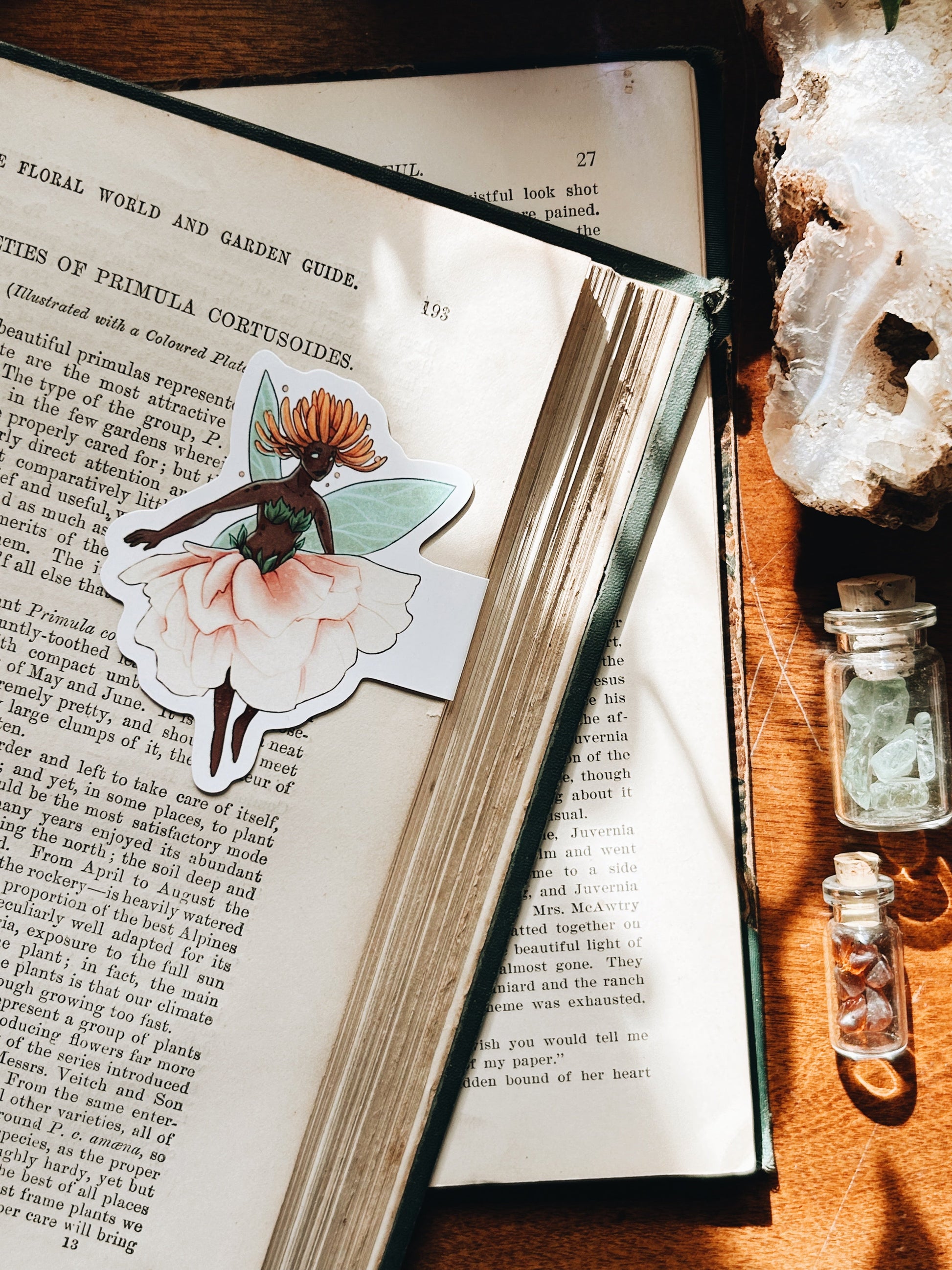 Open book with a decorative sticker of a fairy on a wooden surface with crystals.