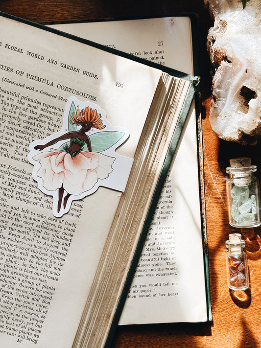 Open book with a decorative sticker of a fairy on a wooden surface with crystals.