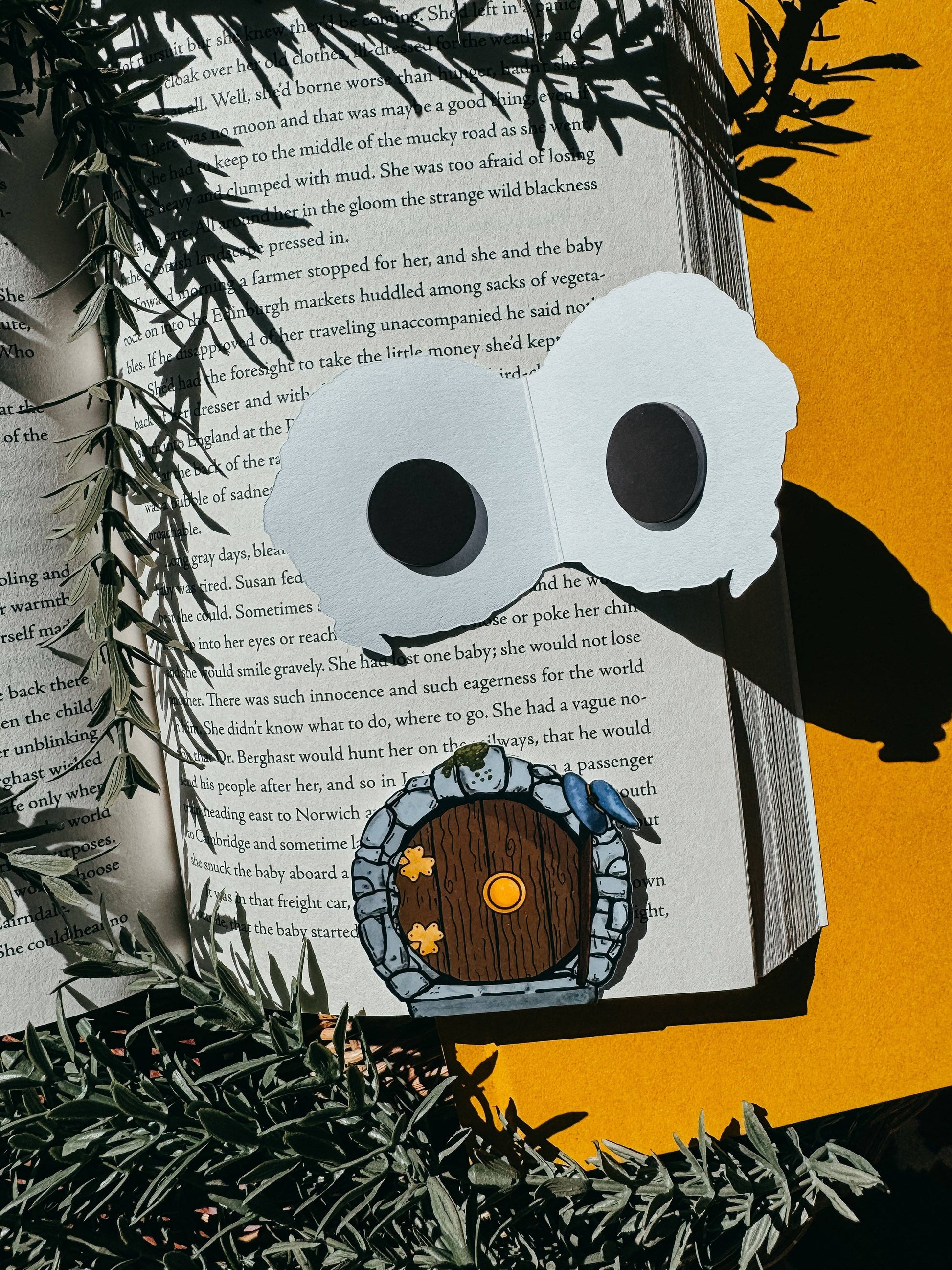 Owl-shaped book mark with a small house design on an open book against an orange background.