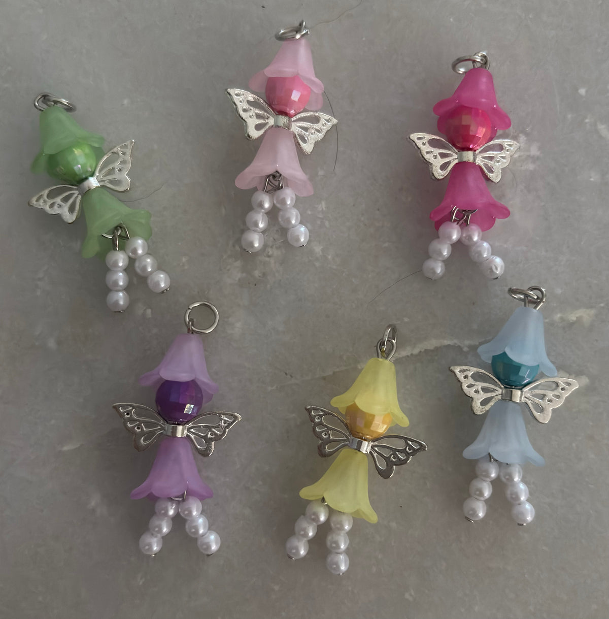 Colorful fairy-shaped charms with butterfly wings on a gray surface