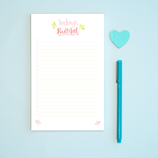 Notepad with 'Today's Bullshit' text, blue pen, and heart-shaped object on a light blue background