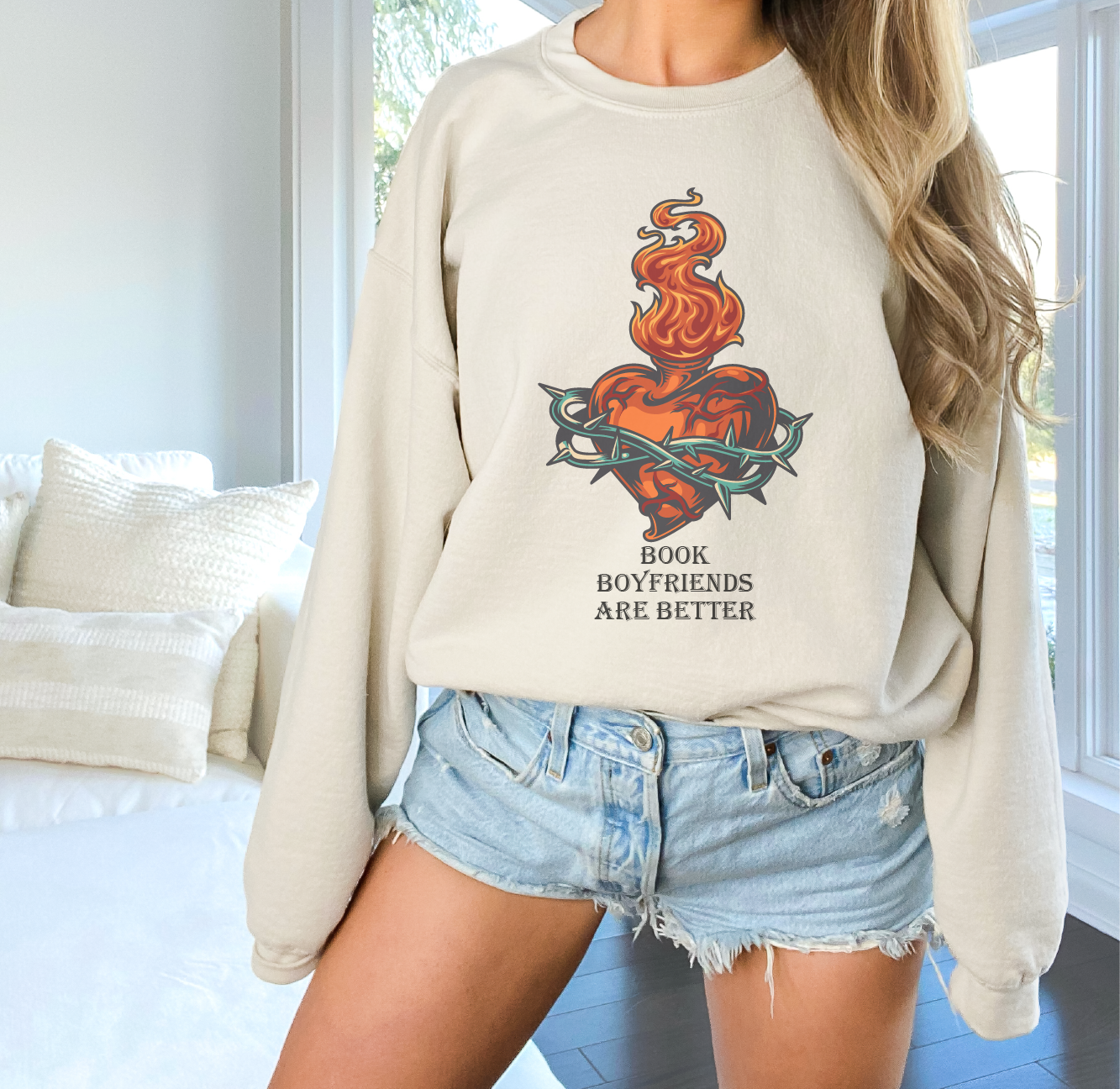 Person wearing a beige sweatshirt with a graphic design and text, standing in a room.