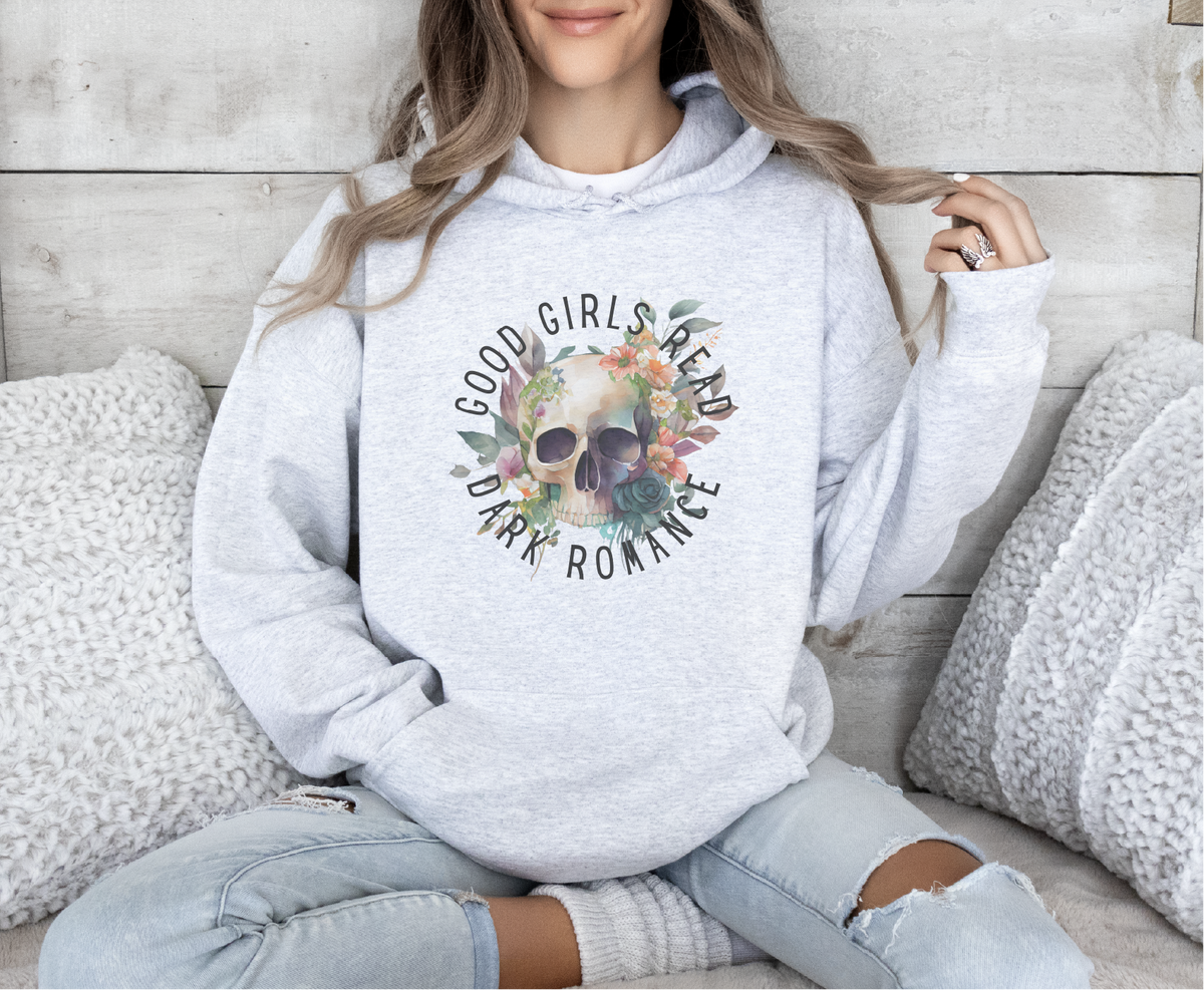 Person wearing a gray hoodie with a skull design and text, sitting on a wooden floor.