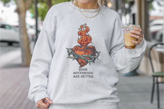 Person wearing a gray sweatshirt with a graphic design and text, holding a coffee cup outdoors.