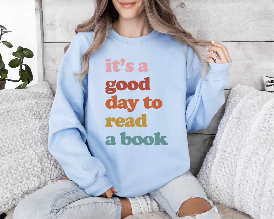 Person wearing a light blue sweatshirt with colorful text, sitting on a couch.
