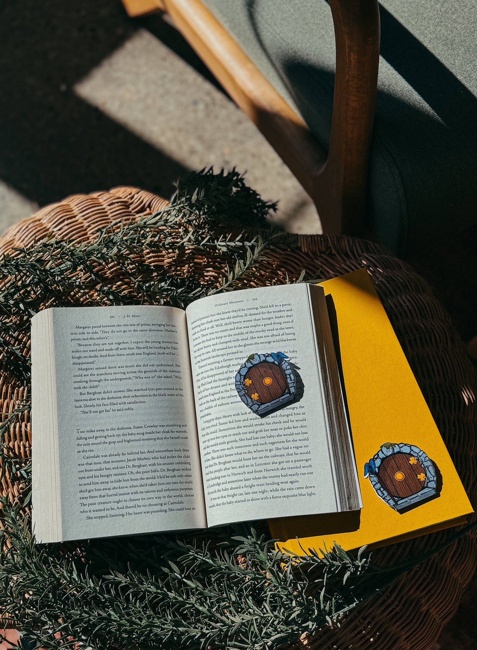 Open book with stickers on a surface, surrounded by greenery