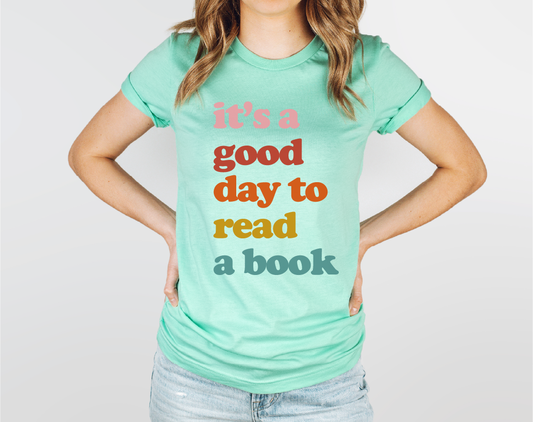 Person wearing a mint green t-shirt with colorful text on a plain background